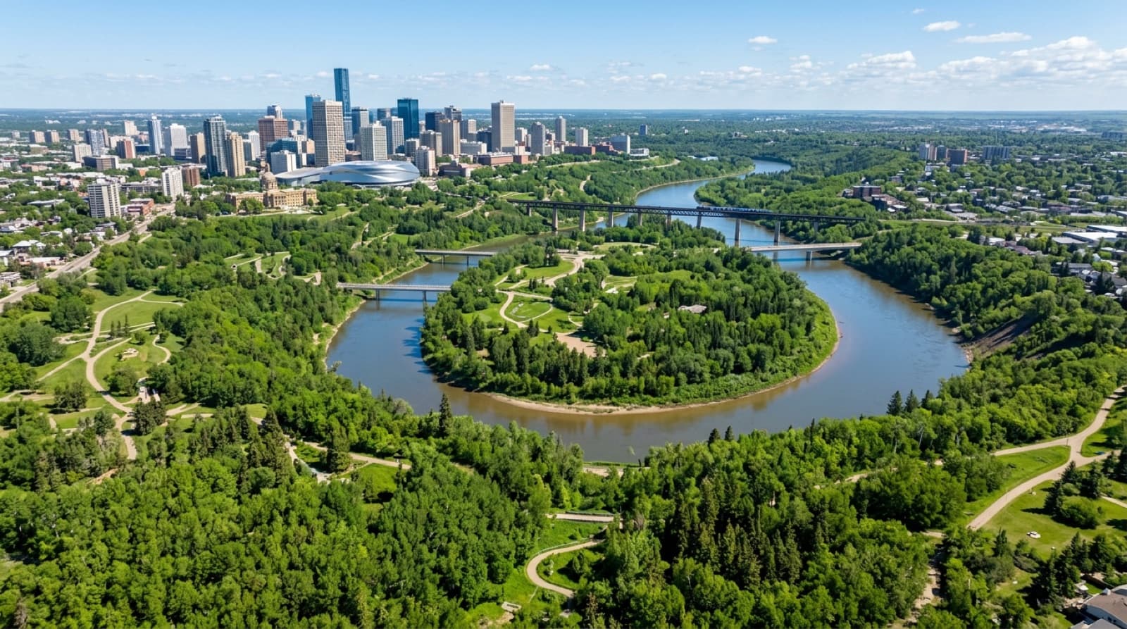 A panoramic view of the North Saskatchewan River Valley running through downtown Edmonton with dense green forested park lands lining the river.